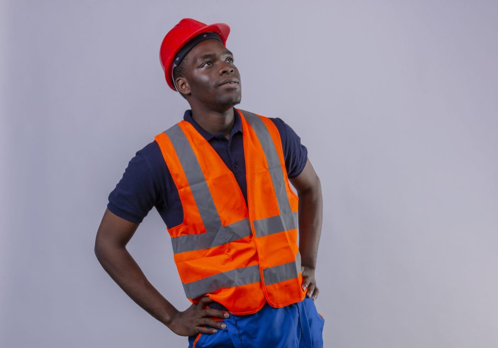 young african american builder man wearing construction vest and safety helmet looking up with serious face standing over white background